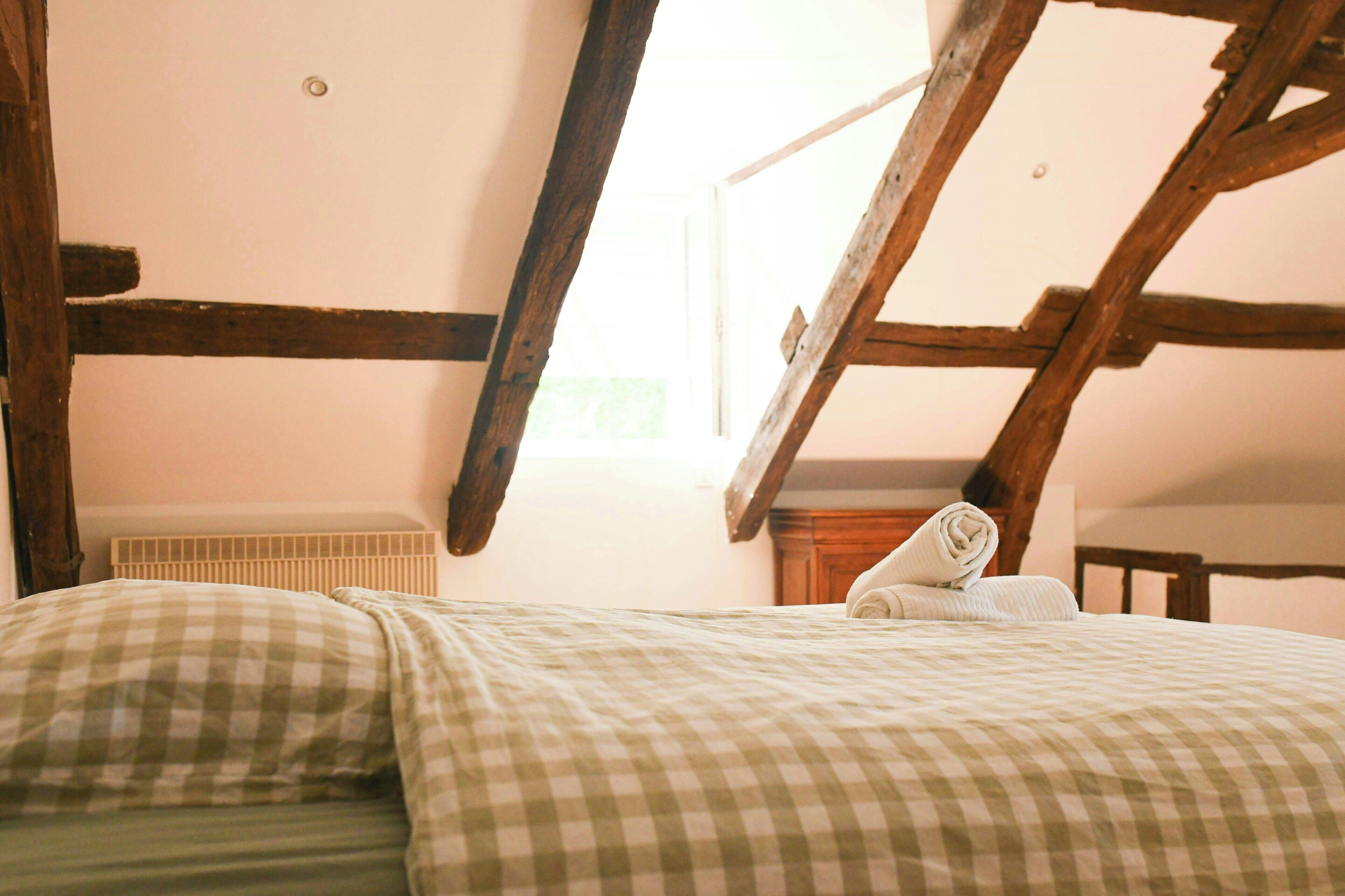 Un dormitorio con techo inclinado, vigas de madera, un radiador y una ventana.