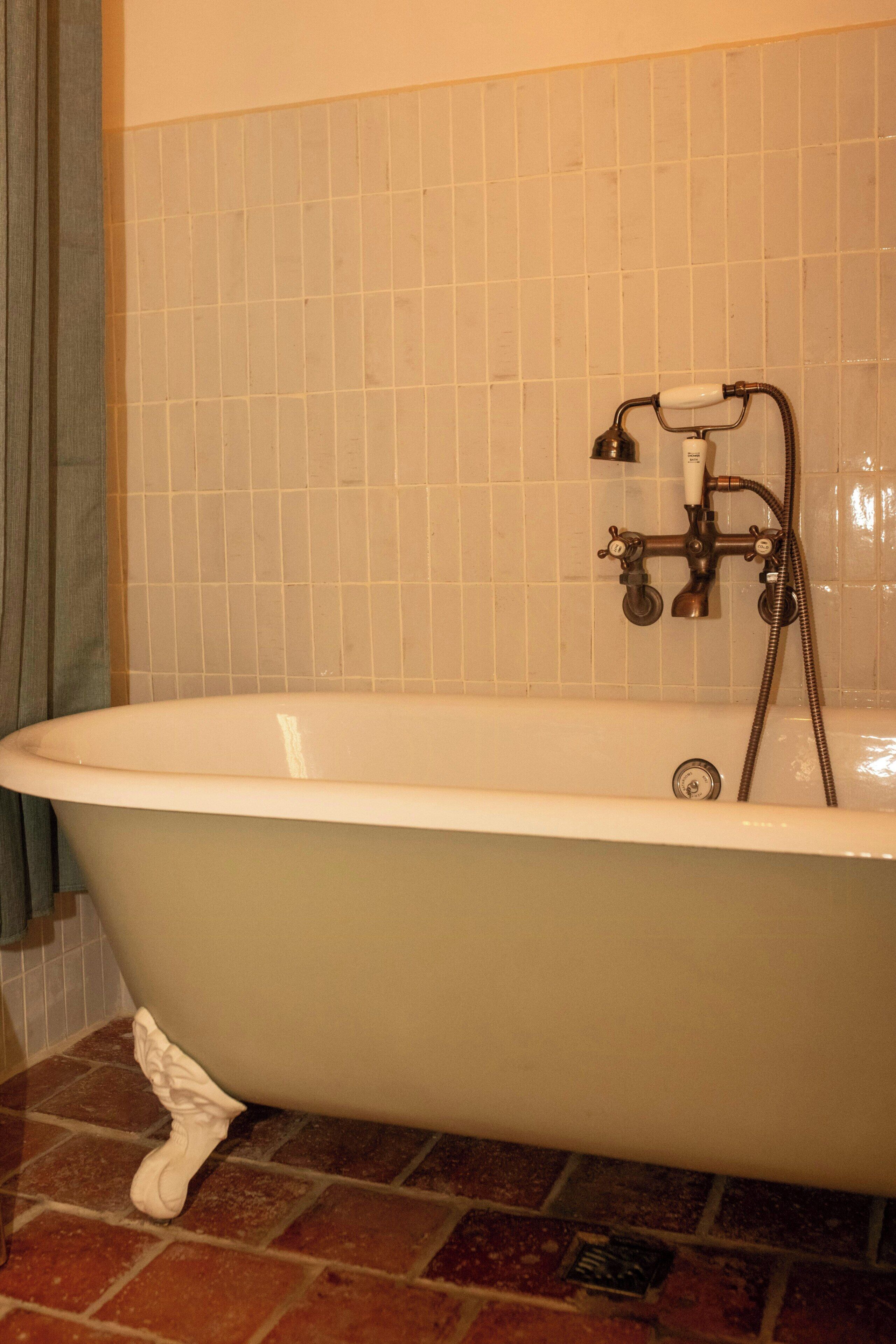 Una bañera con grifo y manguera, frente a una pared de azulejos.