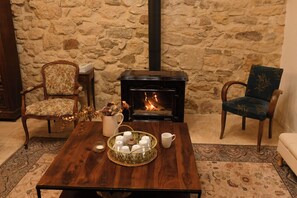 Una habitació acollidora amb una paret de pedra, una llar de foc, dues butaques tapissades, una taula de cafè de fusta amb espelmes i una tassa, i una catifa amb dibuixos.