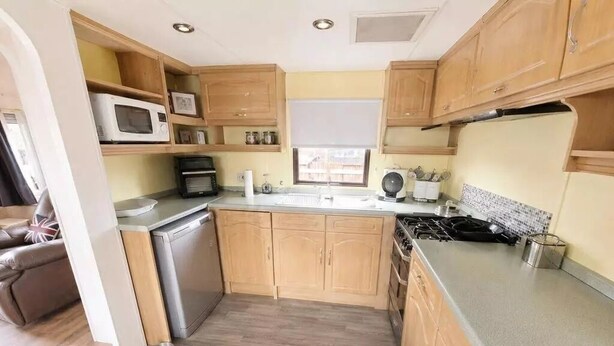 A compact kitchen with wooden cabinets, a microwave, a stove, and a sink. - Riverside Escape - Newark on Trent (Newark)
