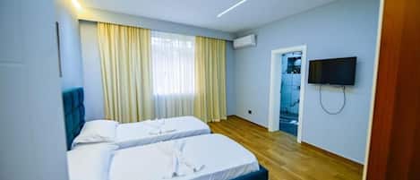 A hotel room with two beds, a television, and a wooden floor.