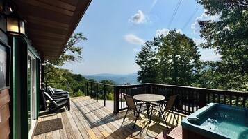 A wooden deck with a hot tub, outdoor seating, and a view of the landscape.