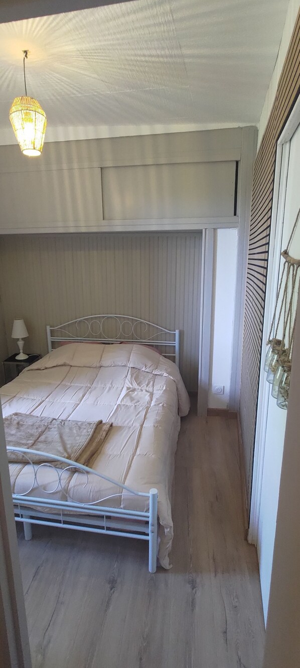 A bedroom with a bed, bedside table, lamp, and a hanging light fixture.