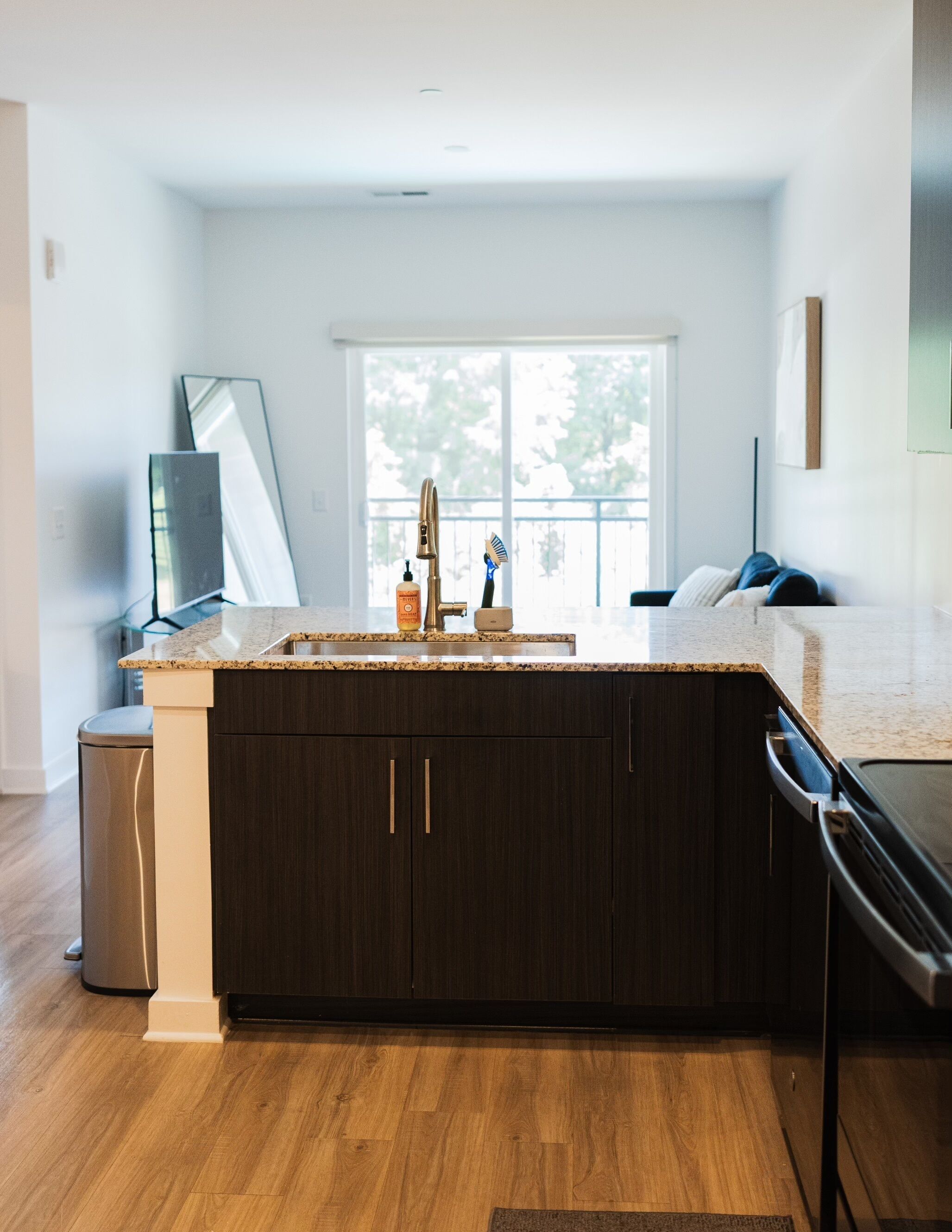 A modern kitchen with dark wood cabinets, a granite countertop, a stainless steel dishwasher, and a window providing natural light.