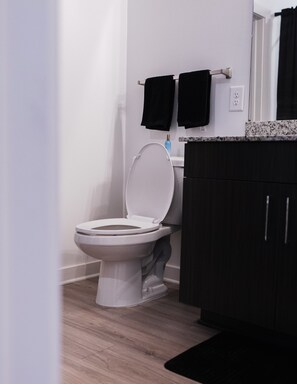Een moderne badkamer met een wit toilet, donkerhouten kastjes en een marmeren aanrechtblad.