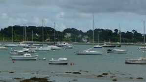 A marina with various boats docked, surrounded by a calm sea and a backdrop of houses and trees. - Apartment in a beautiful house in the countryside near the ocean. (Plévenon)