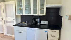 A kitchen with white cabinets, a black countertop, a dishwasher, and a coffee maker. - Apartment in a beautiful house in the countryside near the ocean. (Plévenon)