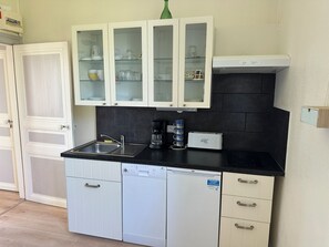 A kitchen with white cabinets, a black countertop, a dishwasher, and a coffee maker. - Apartment in a beautiful house in the countryside near the ocean. (Plévenon)
