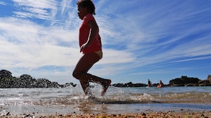 A person running in shallow water near rocks under a clear sky. - Apartment in a beautiful house in the countryside near the ocean. (Plévenon)