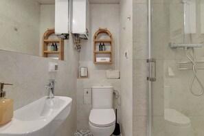 Ein Badezimmer mit Waschbecken, Toilette und Dusche. Es gibt Korbschranke mit Pflegeprodukten.