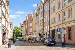 Eine gepflasterte Straße gesäumt von historischen Gebäuden, Außenbestuhlung und einem parkenden Auto.