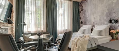 A room with a bed, a dining table with chairs, a chandelier, and a view through large windows with curtains.