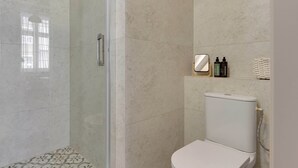 A bathroom with a glass shower enclosure, a toilet, and a shelf with toiletries. - Charm Atelier Apartment 3A | Old Town Ducha Street (Gdańsk)