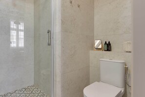 A bathroom with a glass shower enclosure, a toilet, and a shelf with toiletries. - Charm Atelier Apartment 3A | Old Town Ducha Street (Gdańsk)