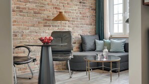 A living room with a brick wall, a sofa, a chair, a small table, and a lamp. - Charm Atelier Apartment 3A | Old Town Ducha Street (Gdańsk)