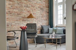 A living room with a brick wall, a sofa, a chair, a small table, and a lamp. - Charm Atelier Apartment 3A | Old Town Ducha Street (Gdańsk)
