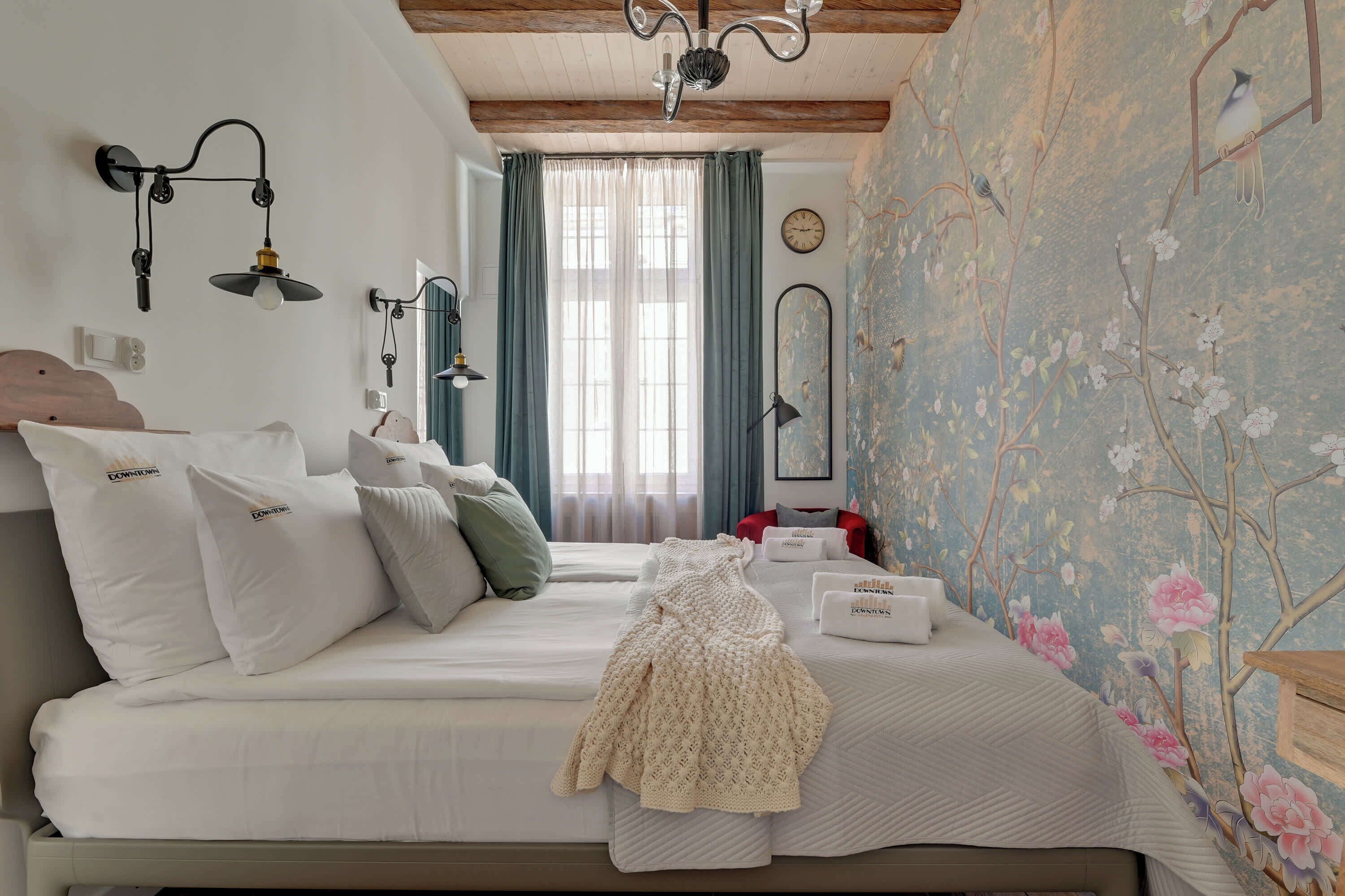 Une chambre avec deux lits, un lustre, une horloge et un papier peint à motifs floraux.