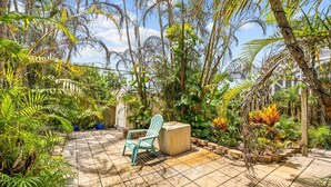 Un espace patio doté d’un sol carrelé, d’une chaise verte et de diverses plantes tropicales.