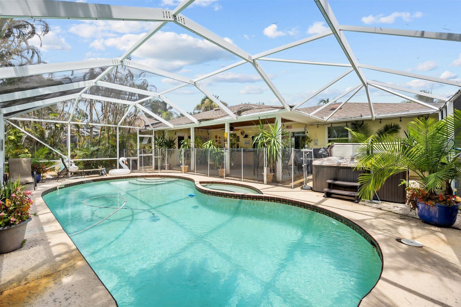 A covered swimming pool with a curved design, surrounded by potted plants and outdoor furniture.