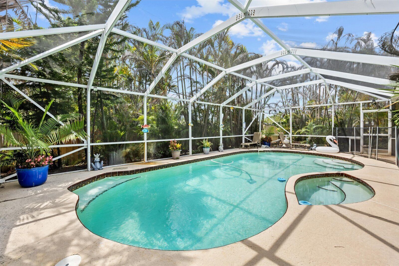 An indoor swimming pool with a glass enclosure, surrounded by potted plants and lounge chairs.