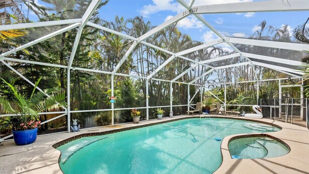 Une piscine intérieure dotée d’une paroi vitrée, entourée de plantes en pot et de chaises longues.