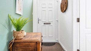 A hallway with a white door, a wooden chest of drawers, a potted plant, a framed picture on the wall, and a textured rug on the floor. - Edinburgh CITY Centre 2BR Apartment (Edinburgh)