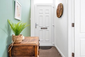 A hallway with a white door, a wooden chest of drawers, a potted plant, a framed picture on the wall, and a textured rug on the floor. - Edinburgh CITY Centre 2BR Apartment (Edinburgh)