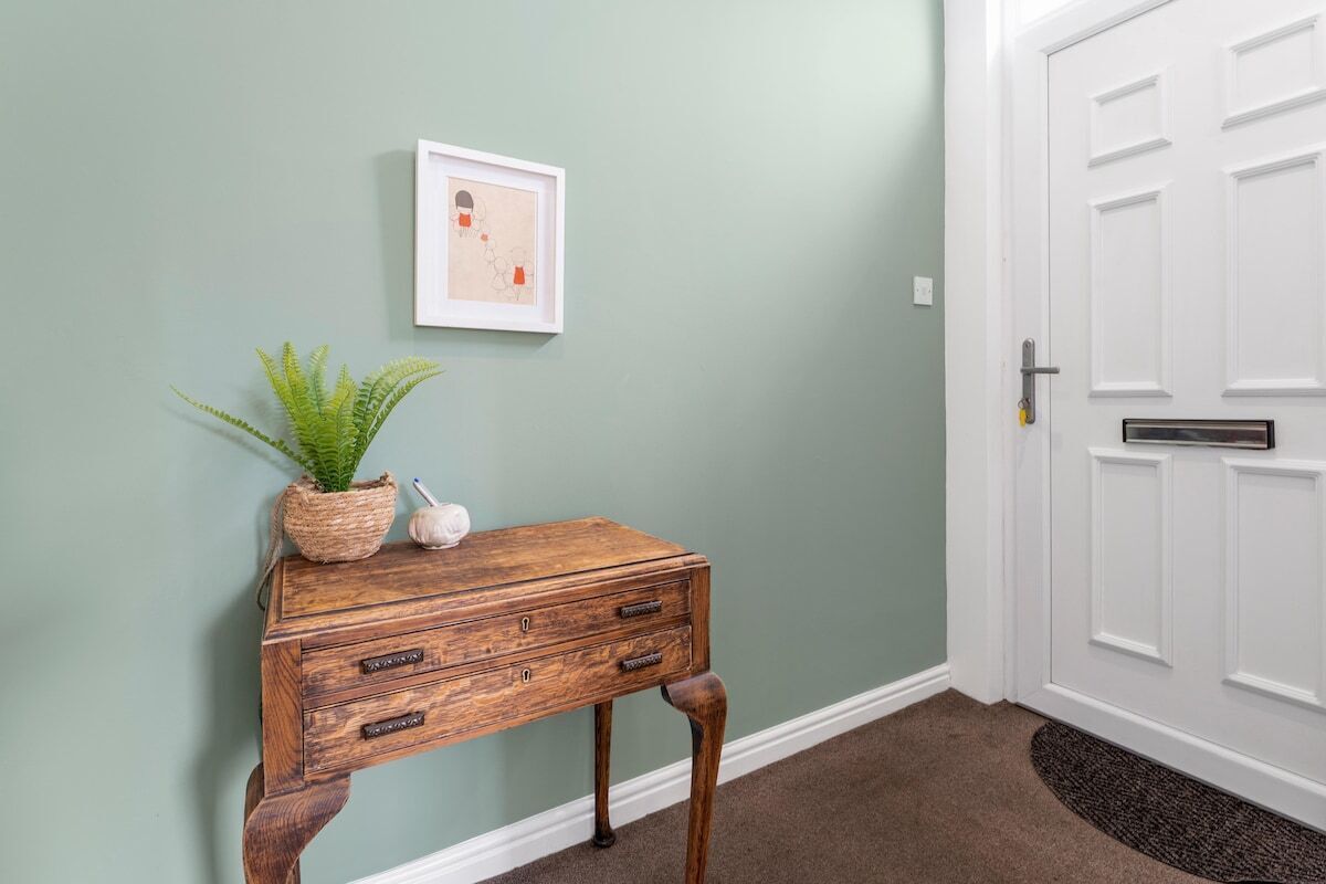 A wooden console table with a potted plant and a small decorative item against a light green wall.