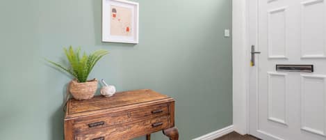 A wooden console table with a potted plant and a small decorative item against a light green wall.