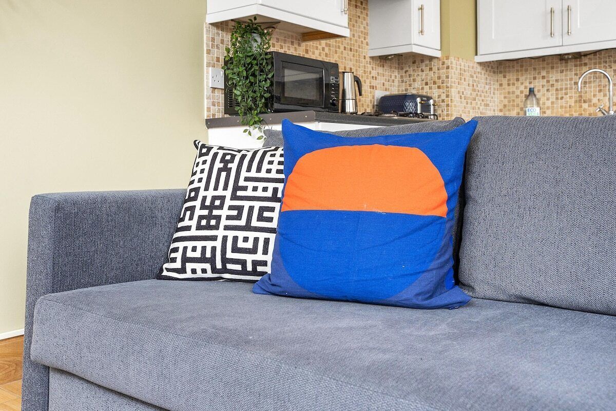 A grey sofa with two decorative pillows, one with a geometric pattern and the other with a blue and orange design.