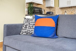 Ein graues Sofa mit zwei Zierkissen, eines mit geometrischem Muster und das andere mit blau-orangem Design.