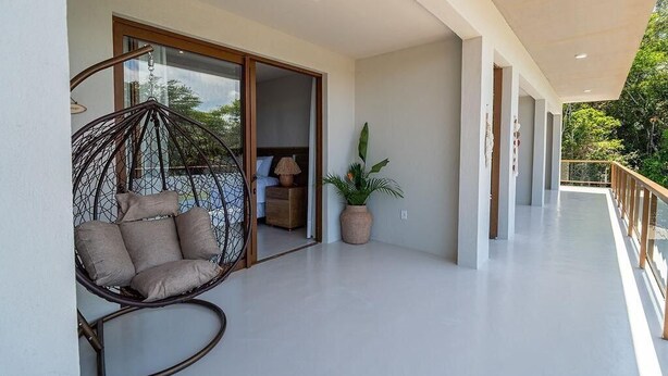 A spacious balcony with a hanging chair, a potted plant, and a glimpse of a bedroom with a bed and nightstand. - 159M- Casa de Luxo em Trancoso-BA  (Porto Seguro)