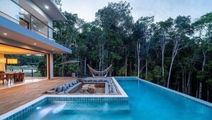 A modern outdoor pool area with a hammock, seating, and a view of a forested area. - 159M- Casa de Luxo em Trancoso-BA  (Porto Seguro)
