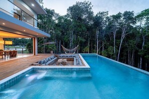 Ein moderner Poolbereich im Freien mit einer Hängematte, Sitzgelegenheiten und Blick auf ein bewaldetes Gebiet.