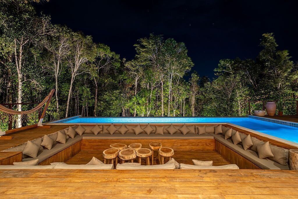 A poolside area with wooden seating and a view of trees at night.