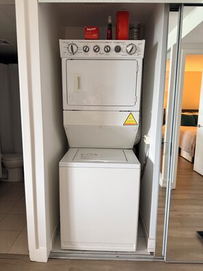 Uma lavanderia compacta com máquina de lavar e secadora de abertura frontal, um sinal de alerta e um frasco de detergente Bounce por cima.