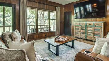 A living room with a large window, a television mounted on the wall, and a wooden cabinet with drawers.
