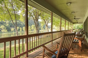 A covered deck with wooden railings overlooking a lake surrounded by trees. - New! Riverfront Trout Fishing White River Retreat (Cotter)