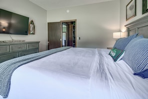 A bedroom with a large bed, a flat-screen TV, a wooden dresser, and a door leading to another room. - New! Riverfront Trout Fishing White River Ozarks (Cotter)