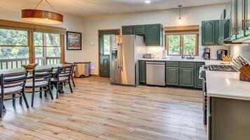 A modern kitchen with a dining area, featuring a large island, stainless steel appliances, and green cabinetry.