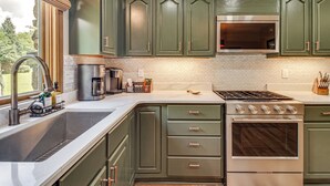 A kitchen with green cabinets, a stainless steel stove, and a large window. - New! Riverfront Trout Fishing White River Ozarks (Cotter)