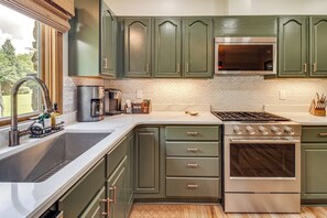 A kitchen with green cabinets, a stainless steel stove, and a large window. - New! Riverfront Trout Fishing White River Ozarks (Cotter)