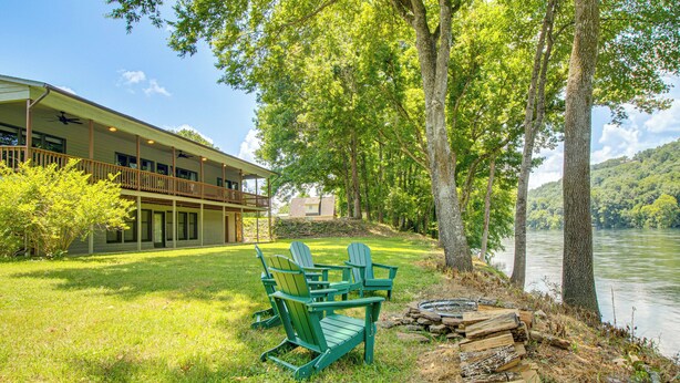 A lakeside lodge with a deck, chairs, and a fire pit. - New! Riverfront Trout Fishing White River Ozarks (Cotter)