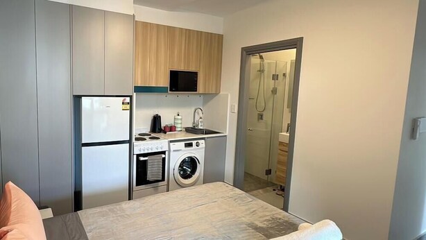 Ein kompaktes Hotelzimmer mit Bett, einer Küchenzeile inklusive Mikrowelle, einer Waschmaschine und einer Duschkabine.