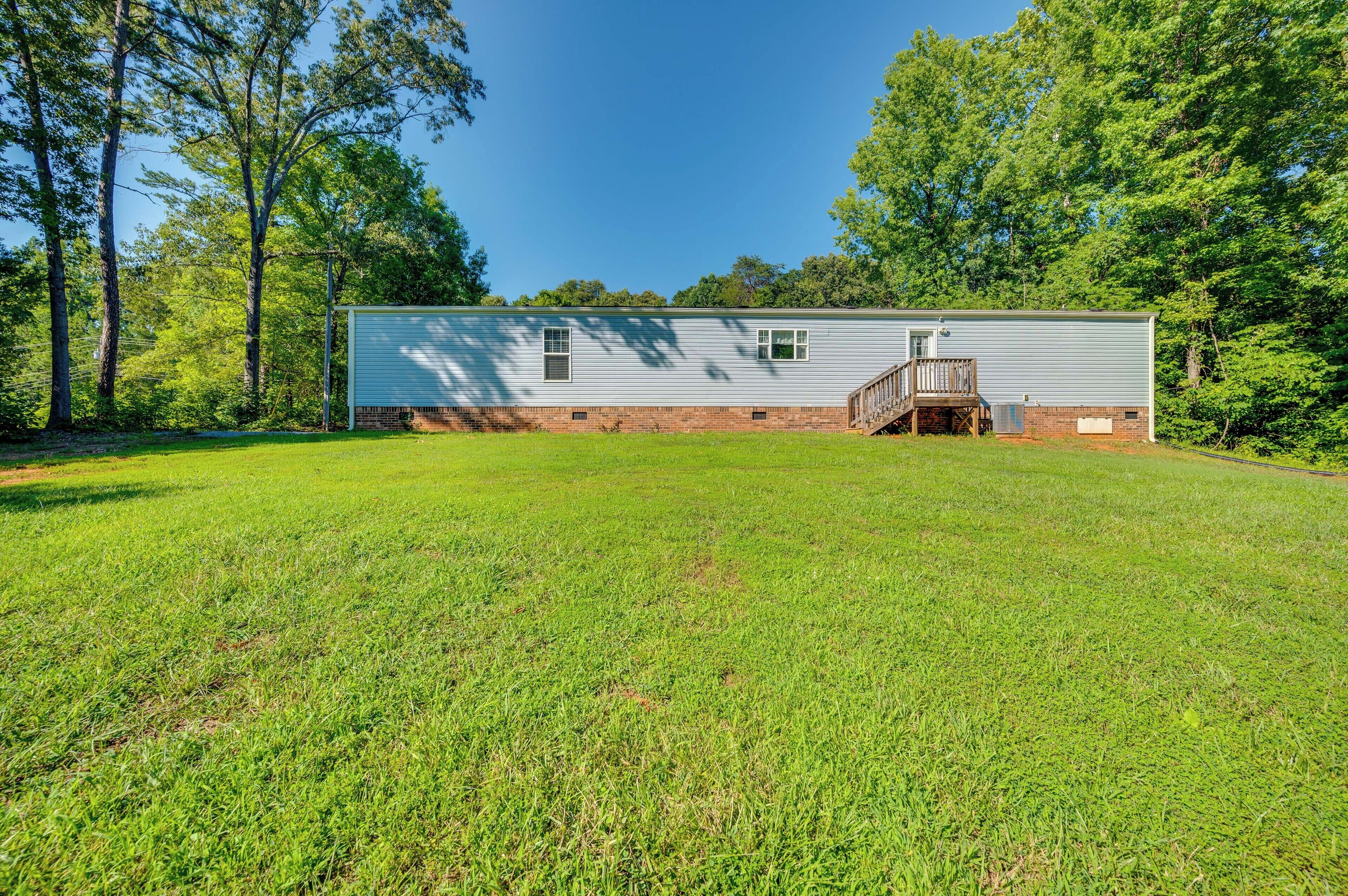 A single-story house with a front porch and a small deck, surrounded by a grassy yard and trees.
