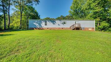 A single-story house with a front porch and a small deck, surrounded by a grassy yard and trees.