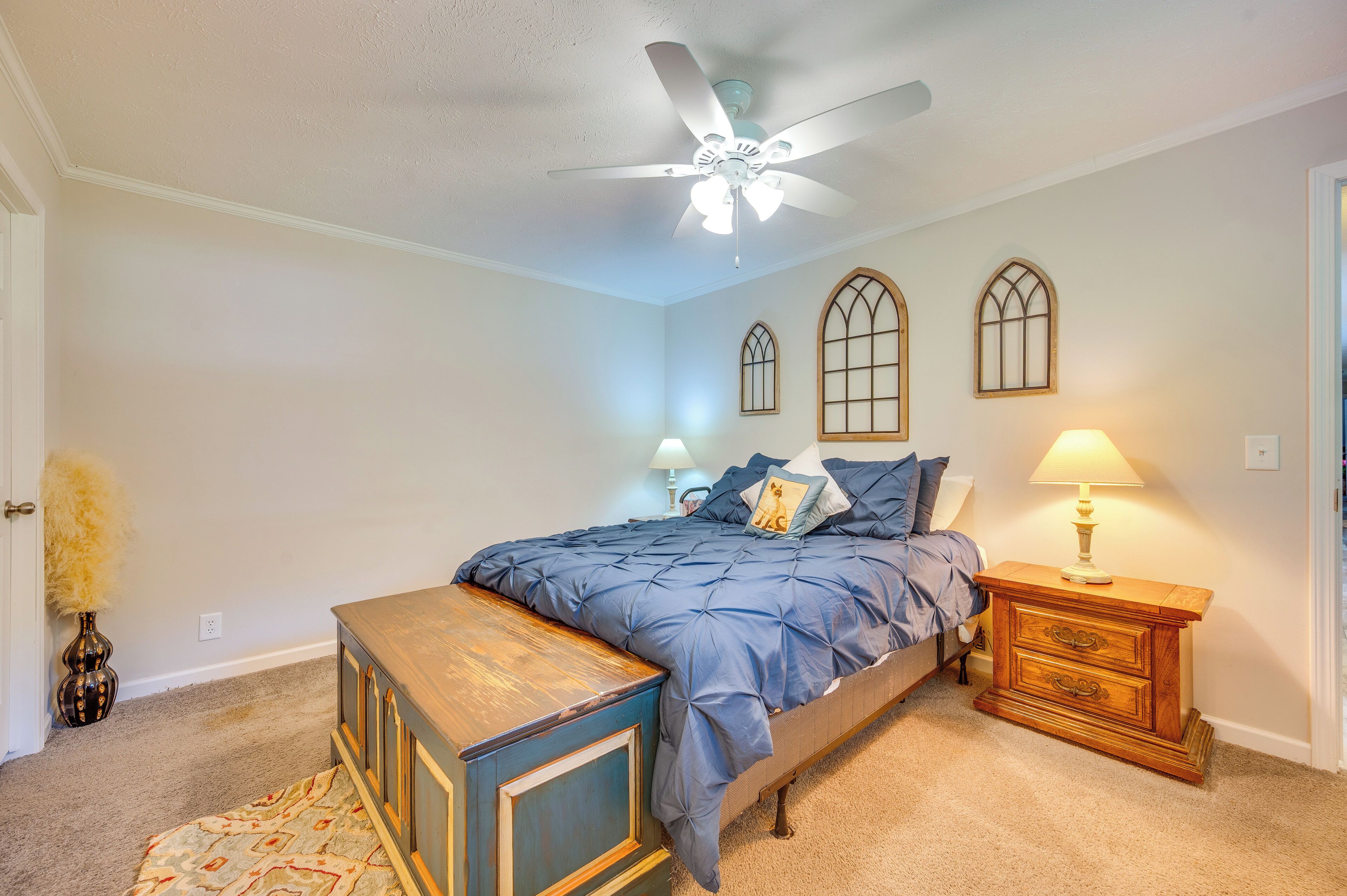 A bedroom with a bed, a nightstand, a dresser, a ceiling fan, and two wall-mounted windows.