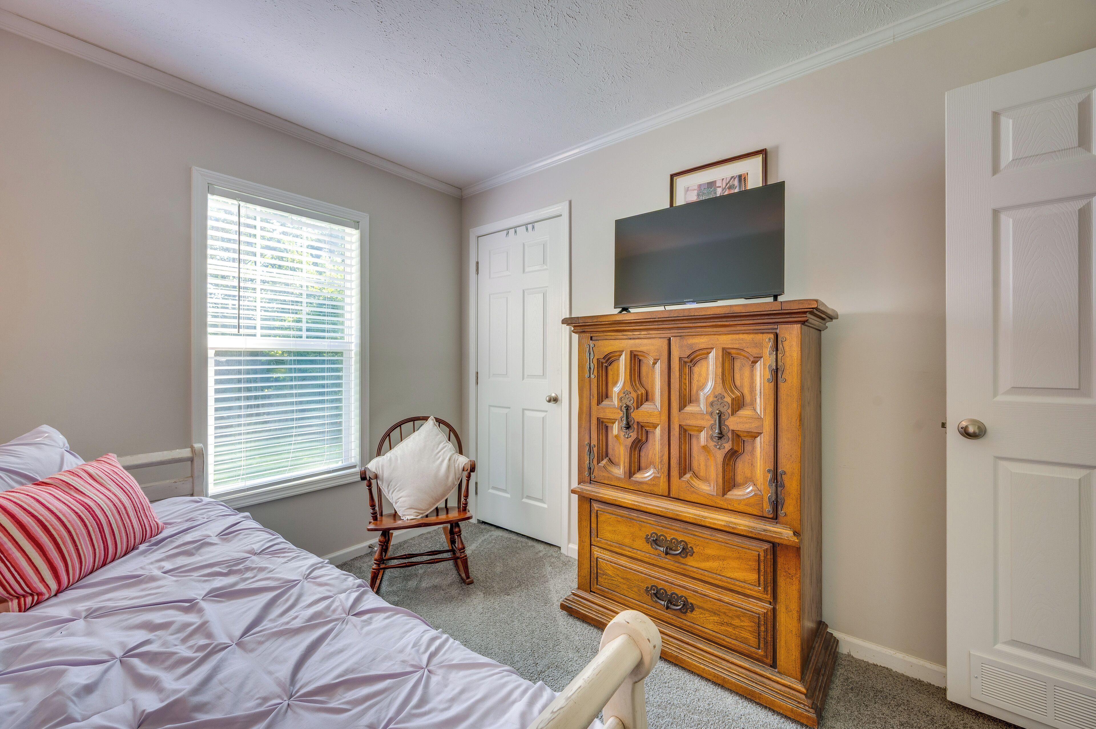 A bedroom with a bed, a wooden dresser, a chair, and a television on top of the dresser.