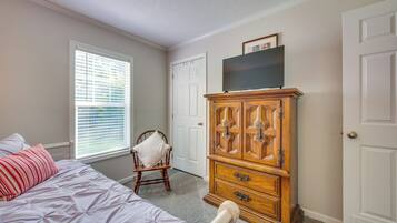 A bedroom with a bed, a wooden dresser, a chair, and a television on top of the dresser.