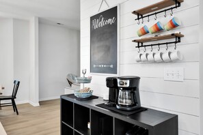 Uma cozinha moderna com cafeteira, um quadro negro e canecas nas prateleiras.